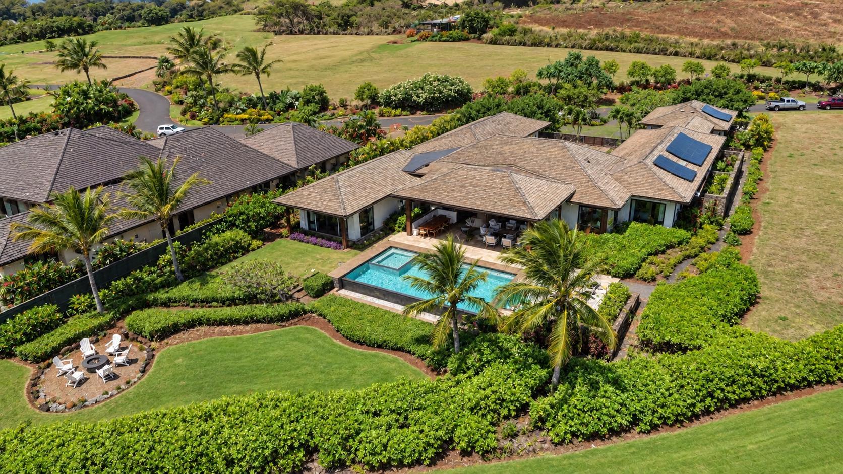 Aerial view of a tropical home with a pool, palm trees, landscaped gardens, and a lawn.